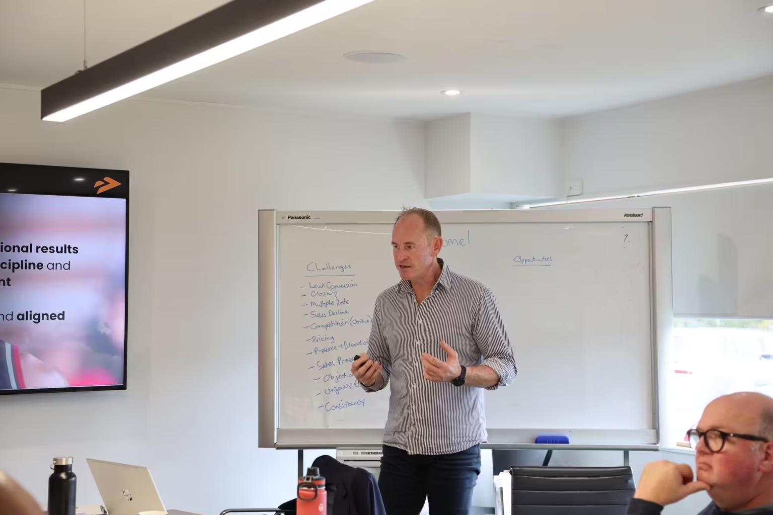Kimble Willis presenting to a sales team, whiteboard behind him listing lead conversion, closing and objections as the challenges on the table